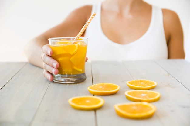 Foto grátis close-up, de, mulher segura, a, vidro, de, suco laranja, com, bebendo, palha, ligado, tabela madeira