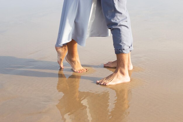 Close-up de pés descalços masculinos e femininos na areia molhada. Homem e mulher andando na praia com uma borda de ondas espumando suavemente por baixo. Férias, conceito de felicidade