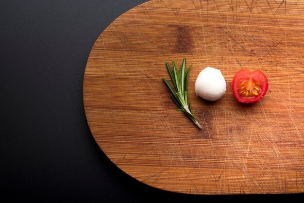 Close-up de queijo fresco; alecrim e meio tomate na tábua de cortar