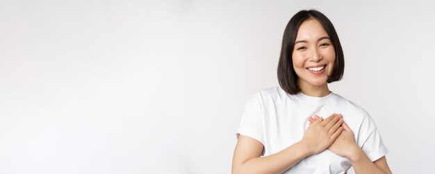 Close-up de sorridente mulher coreana segurando as mãos no cuidado do coração e conceito de amor sentir carinho