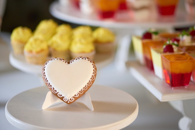 Foto grátis close-up de um biscoito doce de gengibre, coberto com esmalte branco, fica no suporte de madeira em frente ao candybar festivo com cupcakes amarelos e geléias de frutas vermelhas, decorado com framboesas frescas.