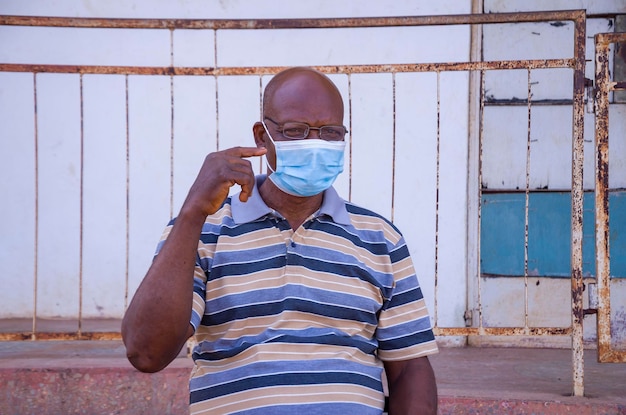Close-up de um homem africano idoso bonito usando máscara facial prevenindo, prevenindo, prevenindo-se do surto na sociedade e apontando para sua máscara facial