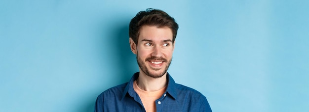 Foto grátis close-up de um homem bonito e confiante com barba olhando para o espaço vazio e sorrindo em pé no ba azul