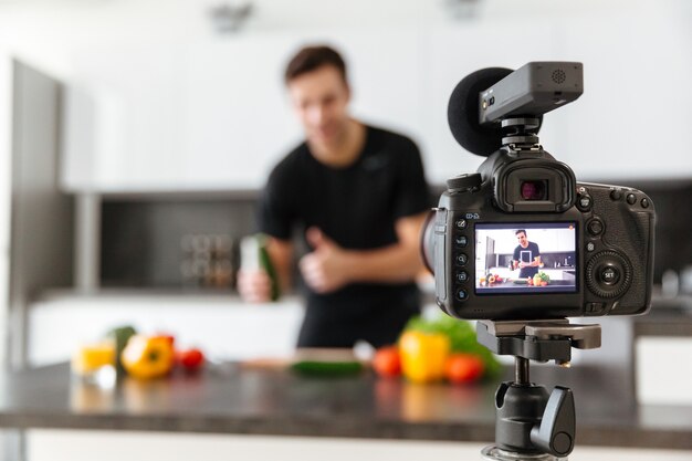 Close-up de uma câmera de vídeo filmando jovem sorridente masculino blogueiro