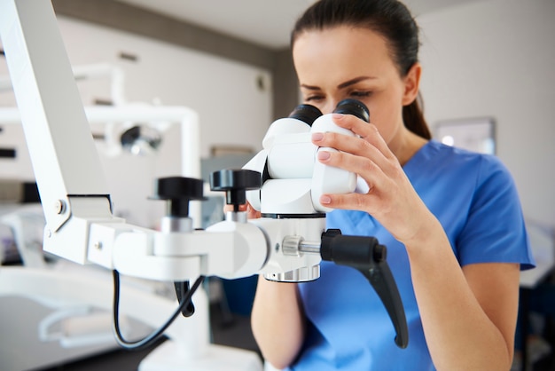 Close-up de uma dentista olhando pelo microscópio odontológico