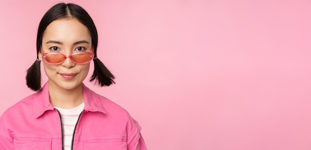 Close-up de uma garota coreana estilosa em óculos de sol sorrindo feliz posando contra pessoas de fundo rosa fa