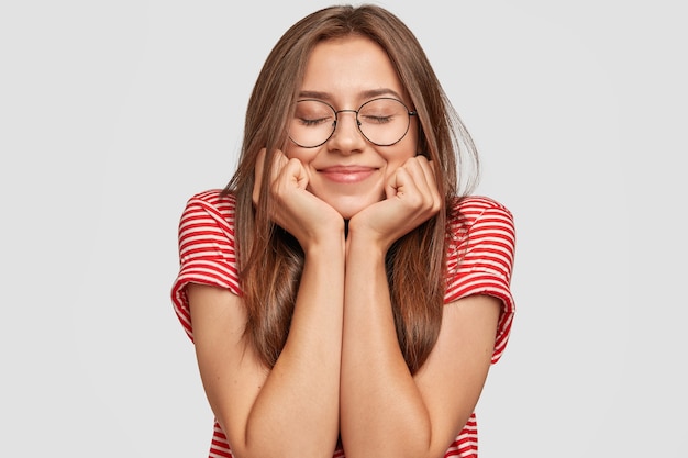 Foto grátis close up de uma linda satisfeita segurando o queixo com as duas mãos, mantendo os olhos fechados