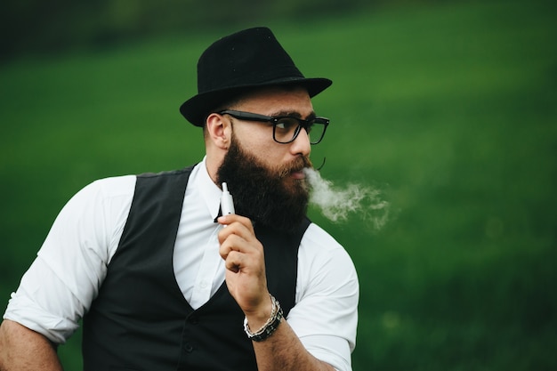 Close-up do homem com chapéu que fuma um charuto eletrônico