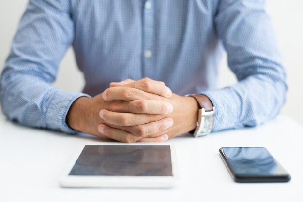 Close up do homem sentado na mesa com tablet e smartphone