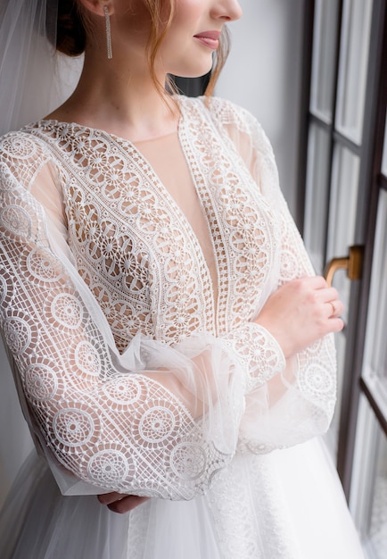 Close-up do vestido chique de macramê branco usado pela noiva em pé perto da janela