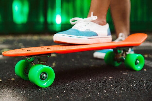 Close-up dos pés de passeios de tênis menina no skate centavo laranja no asfalto