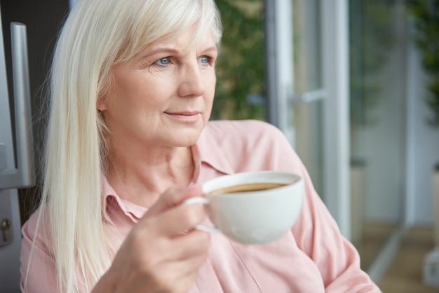 Close-up em uma mulher madura tomando um bom café na varanda