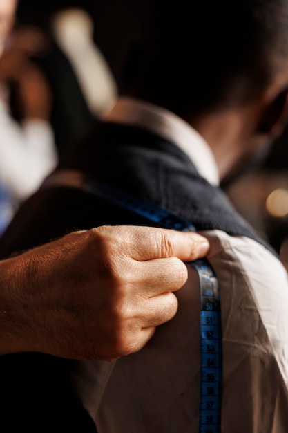 Close-up extremo de um habilidoso terno fazendo o ajuste de tamanho em uma peça de roupa sob medida usando fita métrica. costureiro experiente e preciso ajudando o cliente com traje de alfaiataria feito sob medida