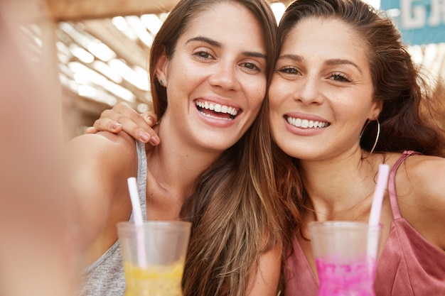 Foto grátis close-up foto de lindas irmãs se abraçando e sorrindo alegremente, faça uma selfie quando passar o tempo livre no refeitório