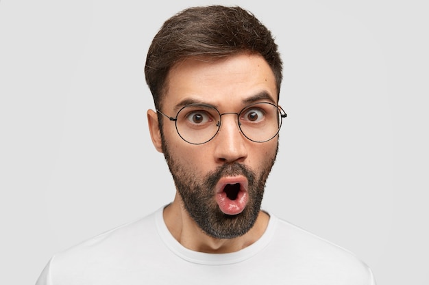 Close-up foto de um jovem bonito e atraente com os olhos cheios de descrença, exclamando inesperadamente