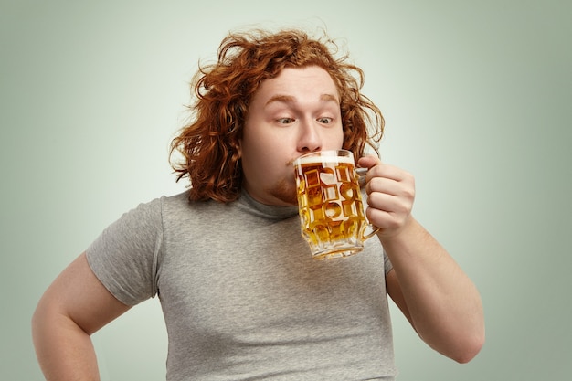 Close-up foto de uma ruiva gorda engraçada bebendo cerveja gelada de vidro