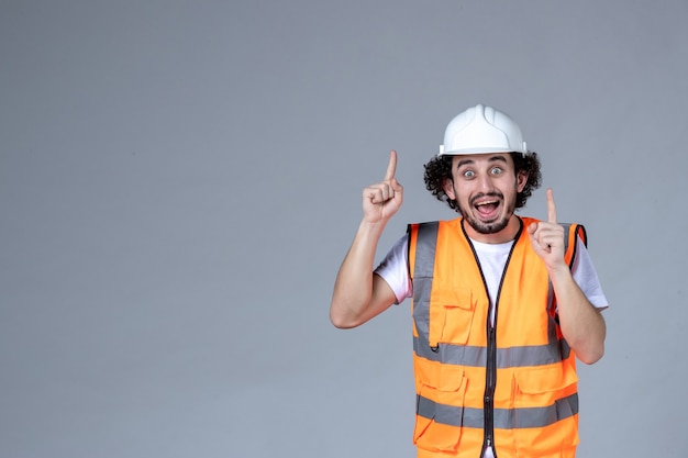 Close-up foto do arquiteto chocado no colete de advertência com capacete de segurança e apontando para cima sobre a parede de onda cinza