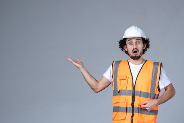 Close-up foto do arquiteto surpreso com colete de advertência com capacete de segurança e apontando algo sobre a parede de onda cinza