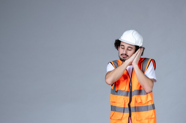 Close-up foto do sonolento construtor masculino em colete de advertência com capacete de segurança na parede de onda cinza