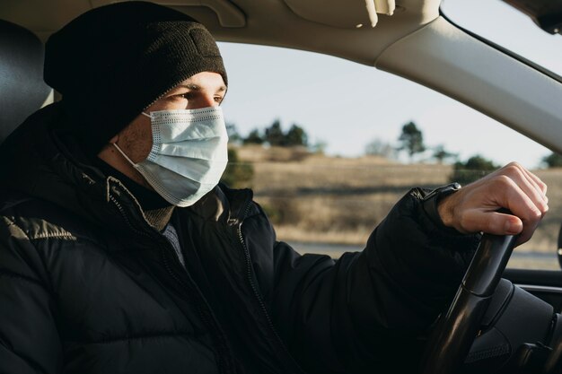 Close-up homem dirigindo com máscara de proteção