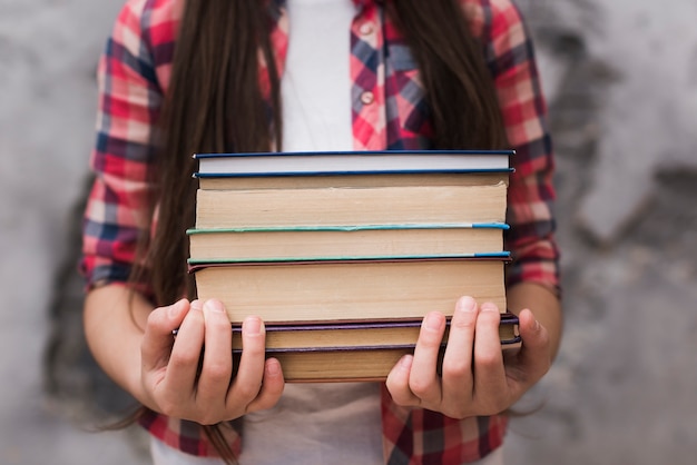 Close-up jovem garota segurando uma pilha de livros