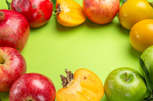 Close-up lateral com frutas coloridas romã maçãs caquis e folhas na mesa