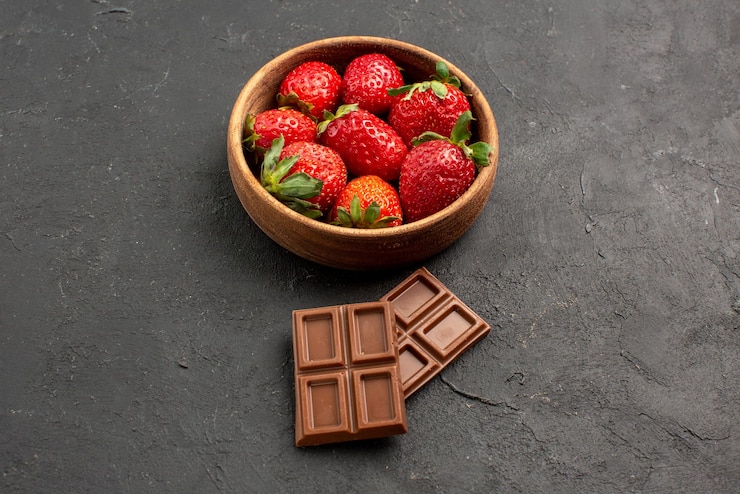 Foto grátis close-up lateral de morangos em uma tigela com barras de chocolate ao lado dos morangos em uma tigela na mesa escura