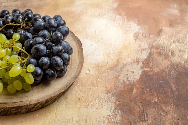 Foto grátis close-up lateral de uvas com cachos de uvas verdes e pretas na tábua de corte