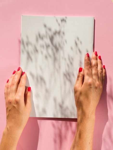Close-up mãos segurando um livro branco com sombras