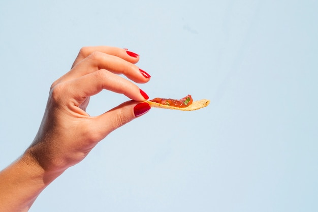 Close-up mulher segurando tortilla chips com fundo azul