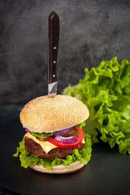Close up shot de faca em delicioso sanduíche de carne e verde na bandeja preta do lado esquerdo em superfície desfocada com espaço livre