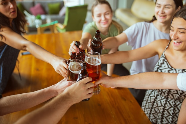 Close up tilintando. Grupo de jovens amigos bebendo cerveja, se divertindo, rindo e comemorando juntos.