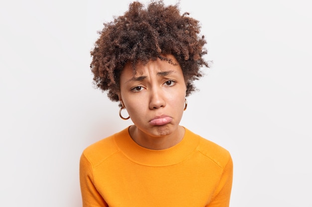 Close-up tiro de descontentamento triste mulher afro-americana sendo insatisfeito ofendido por alguém vestido com jumper laranja isolado sobre a parede branca sente arrependimento e tristeza. emoções negativas