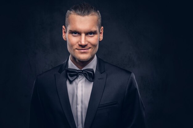 Close-up, um retrato de um homem bonito e elegante sorridente em um elegante terno preto sobre um fundo escuro.