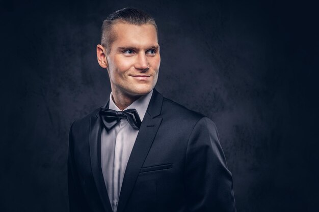 Close-up, um retrato de um homem bonito e elegante sorridente em um elegante terno preto sobre um fundo escuro.