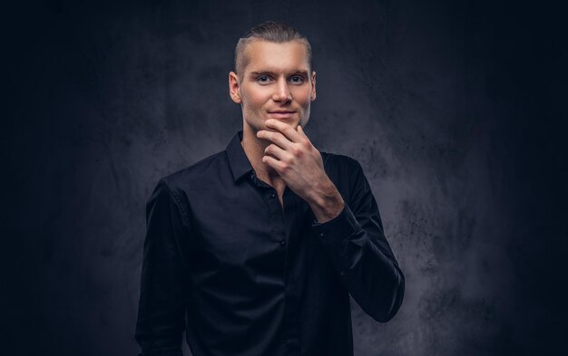 Close-up, um retrato de um homem bonito em poses de camisa preta contra um fundo escuro, de pé no estúdio.