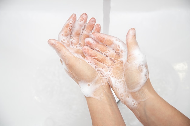 Close-up, uma mulher está lavando a espuma de sabão das mãos com água corrente.
