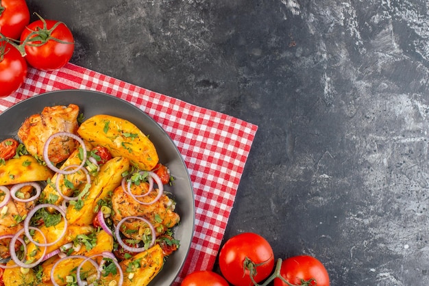 Close-up vista da deliciosa refeição de frango com batatas e legumes verdes em tomates de toalha despojados vermelhos dobrados com caules em fundo de cor escura com espaço livre