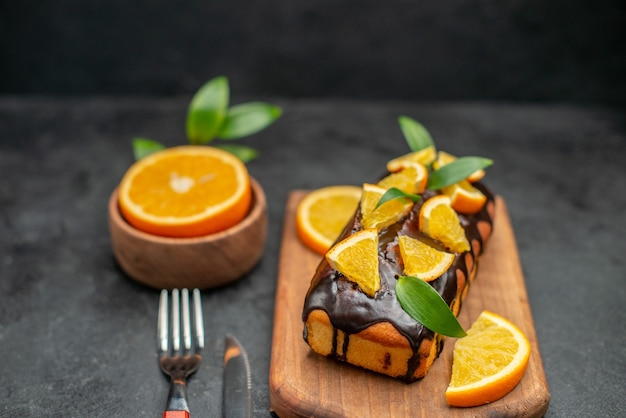 Close-up vista de bolos macios a bordo e corte laranjas com folhas na mesa escura