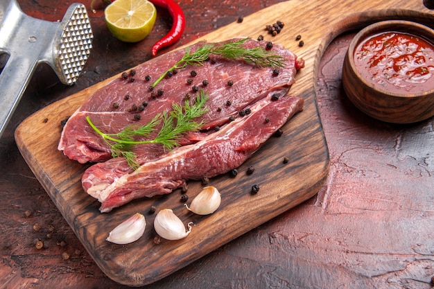 Close-up vista de carne vermelha em uma tábua de corte de madeira e garfo e faca de garrafa de óleo de pimenta verde de alho em fundo escuro