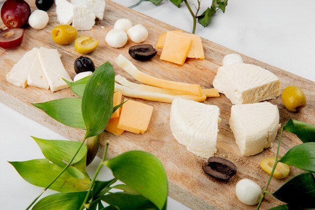 Close-up vista de diferentes tipos de queijo com pedaços de uva azeitonas na tábua em branco decorado com folhas