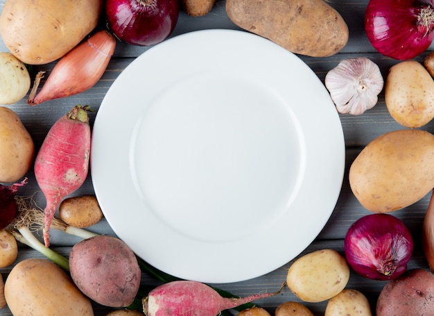 Close-up vista de legumes como alho de batata de cebola rabanete com prato vazio no centro