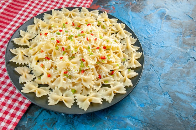 Close-up vista de macarrão farfalle italiano cru em toalha vermelha despojada no lado esquerdo em fundo azul