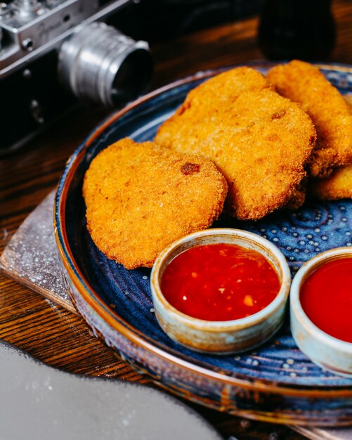 Close-up vista de nuggets de frango, servidos com molho de pimenta doce ketchup e maionese na bandeja no escuro