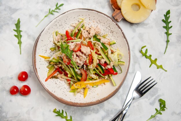 Close-up vista de uma deliciosa salada de frango com vegetais, tomates e talheres de abacaxi secos em uma superfície branca manchada