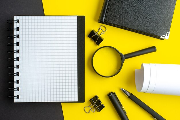 Close-up vista do caderno espiral branco em branco lupa canetas em fundo preto e amarelo misturar cores