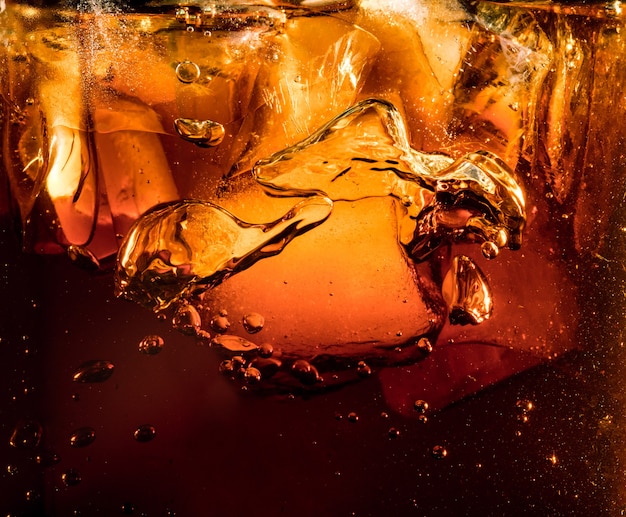 Close-up vista dos cubos de gelo em fundo escuro de cola. Textura de refrigerar a bebida doce do verão com espuma e bolhas macro na parede de vidro. Fizzing ou flutuando até o topo da superfície.