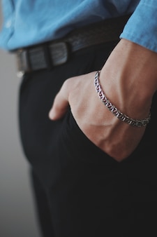 Close vertical de um homem usando uma pulseira de prata com as mãos nos bolsos