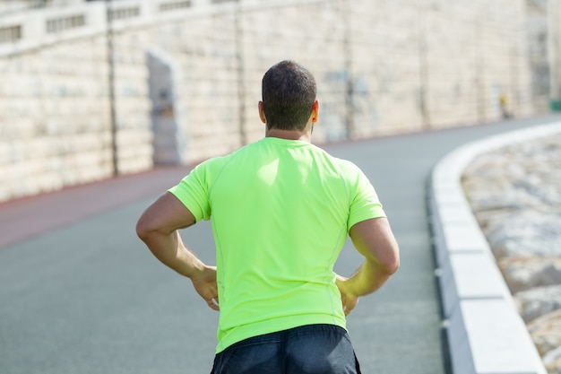 Closeup back view of strong man running on road