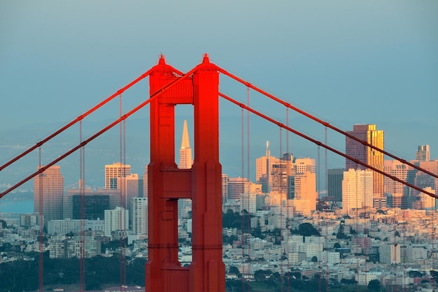 Closeup da ponte Golden Gate com o centro de São Francisco ao pôr do sol.